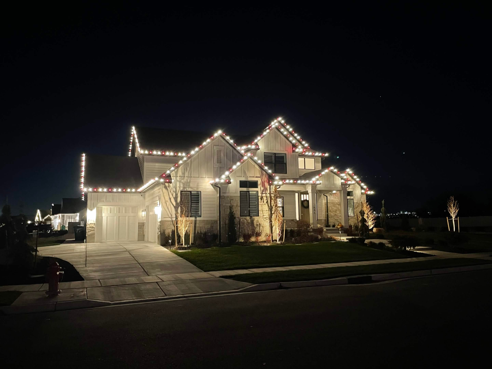 Craftsman-style Utah home outlined in red and warm white Christmas lighting at night
